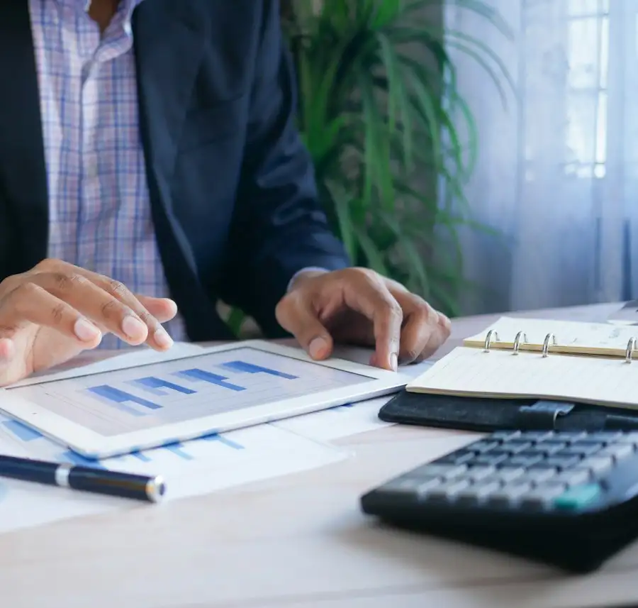 Consultor analisando gráficos no tablet com calculadora e caderno de anotações